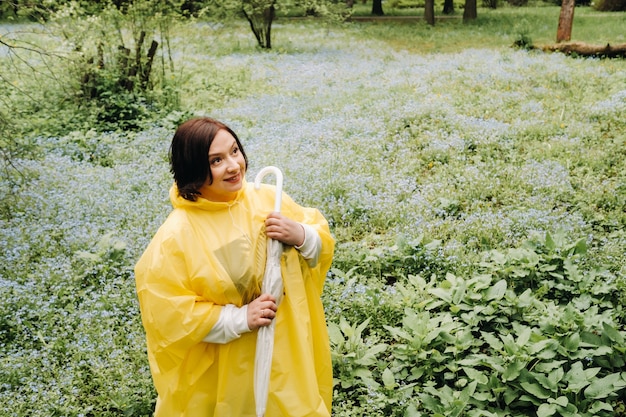 Une femme vêtue d'un imperméable jaune se promène dans le parc et le jardin en été.