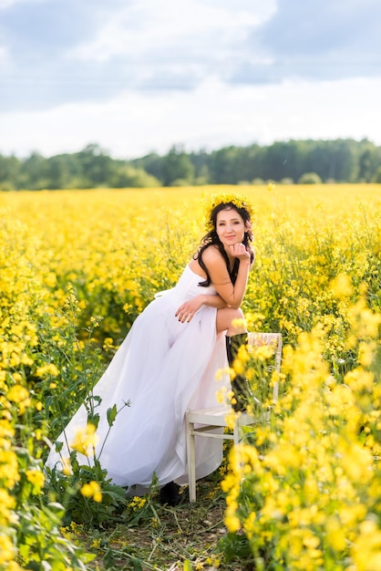 Femme vêtue d'une longue robe blanche et de bottes noires est assise dans un champ de colza La fille aime la nature et la liberté