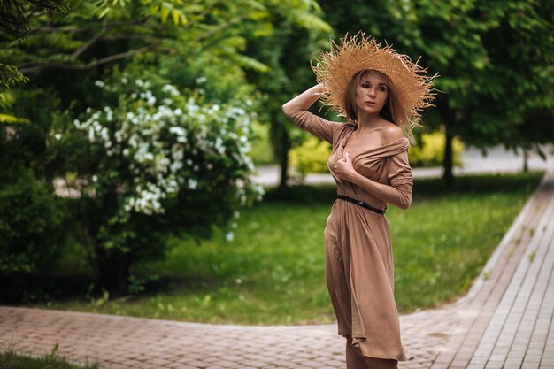 Une femme vêtue d'une longue robe marron et d'un chapeau de paille se promène dans un parc d'été