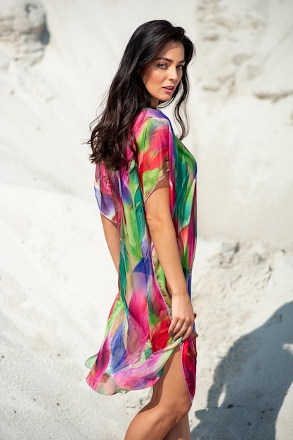 Une femme vêtue d'une robe colorée se tient dans le sable.