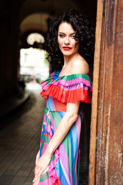 Une femme vêtue d'une robe colorée se tient devant une porte.