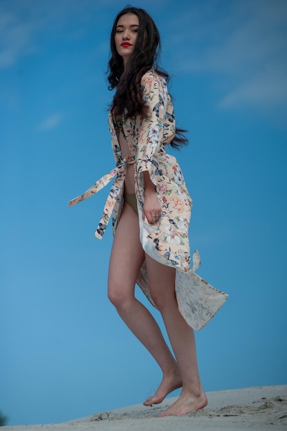 Une femme vêtue d'une robe à fleurs marche sur un fond de ciel bleu.