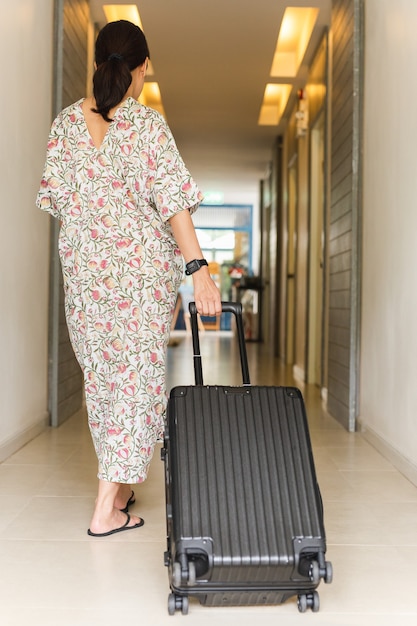 Femme vêtue d'une robe longue marchant avec des bagages dans un couloir de l'hôtel.