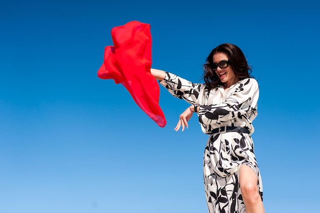 Une femme vêtue d'une robe avec des lunettes de soleil et un chiffon rouge à la main