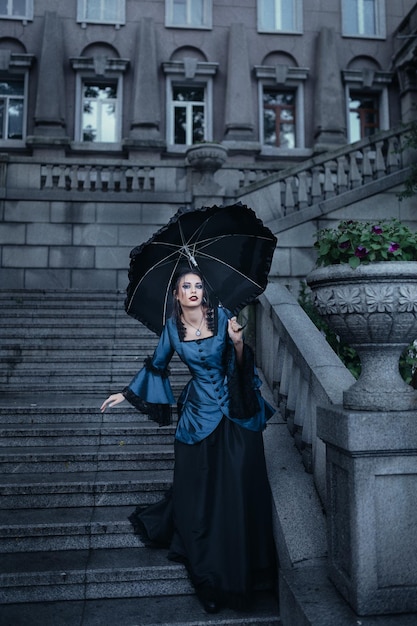 Une femme vêtue d'une robe victorienne bleue se tient près du vieux bâtiment