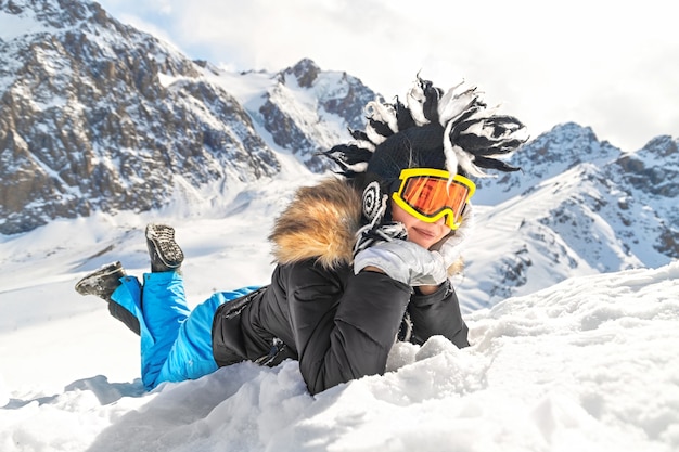 femme vêtue de vêtements d'hiver lunettes de portrait et chapeau d'hiver allongé sur la neige au sommet de la montagne