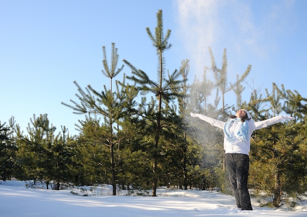 Femme vêtue de vêtements d'hiver, se tient parmi les pins et jette de la neige. Photo pleine hauteur, mains levées