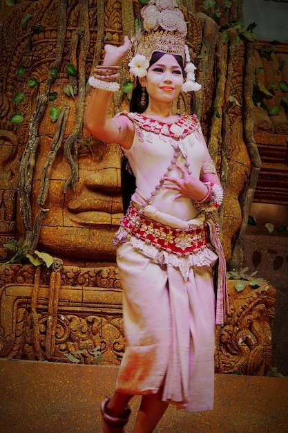 Une femme vêtue de vêtements traditionnels dansant contre une statue.