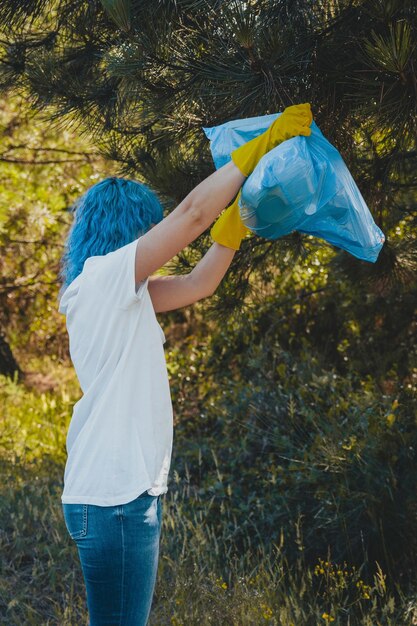 Femme vidant le sac à ordures en plastique dans un environnement vert - concept de pollution plastique