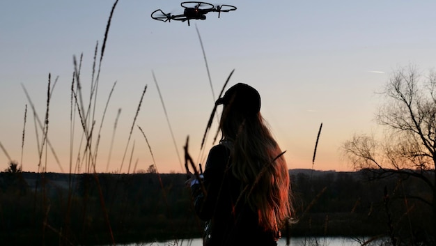 Femme vidéaste pilote un quadricoptère au coucher du soleil Silhouette femme fille d'un pilote et d'un drone