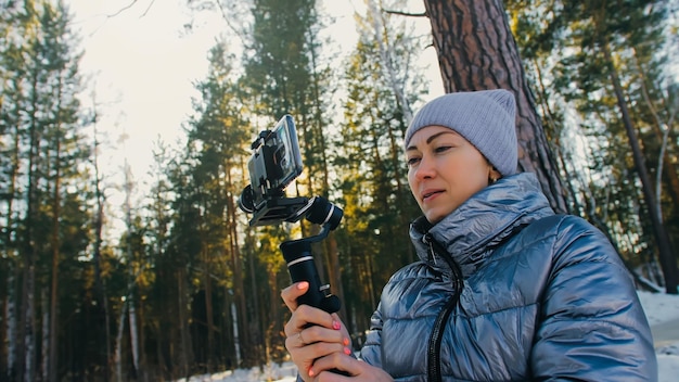 La femme vidéographe professionnelle tenant un smartphone sur un dispositif de stabilisation de cardan à 3 axes dans l'équipement professionnel d'hiver aide à faire une vidéo de haute qualité sur le téléphone