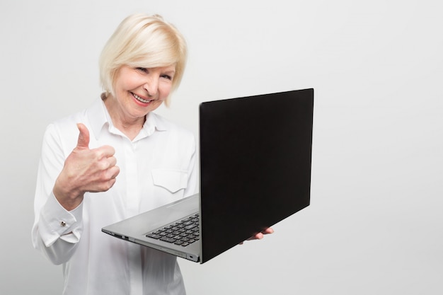 Une femme vieille mais moderne tient un nouvel ordinateur portable. Elle aime l'utiliser. La dame préfère tout savoir sur les nouvelles technologies et les dernières nouvelles sur les équipements informatiques.