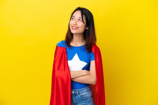 Femme vietnamienne de super héros isolée sur fond jaune en levant tout en souriant