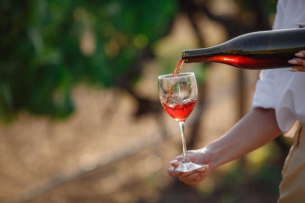 Femme vigneronne dégustant du vin rouge dans un verre dans un vignoble. fond de vignobles au coucher du soleil. Plan macro sur une main de sommelier qui tient le verre à vin