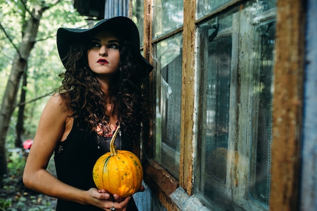 Femme vintage comme sorcière posant avec citrouille dans les mains dans le contexte d'un lieu abandonné à la veille d'Halloween