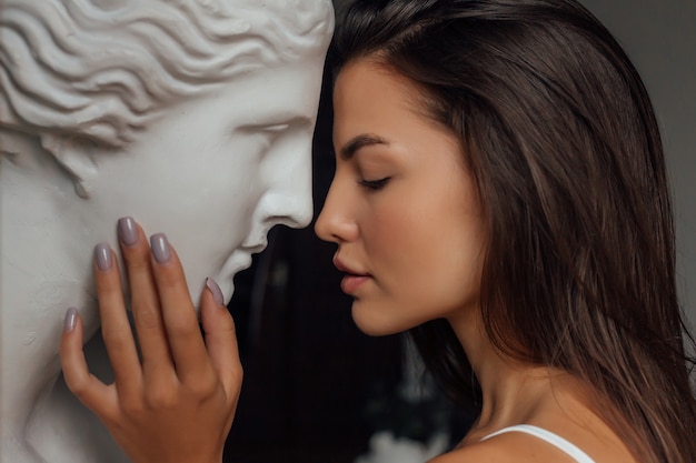 Une femme avec un visage et un corps bien soignés se tient près du buste d'une sculpture de femme