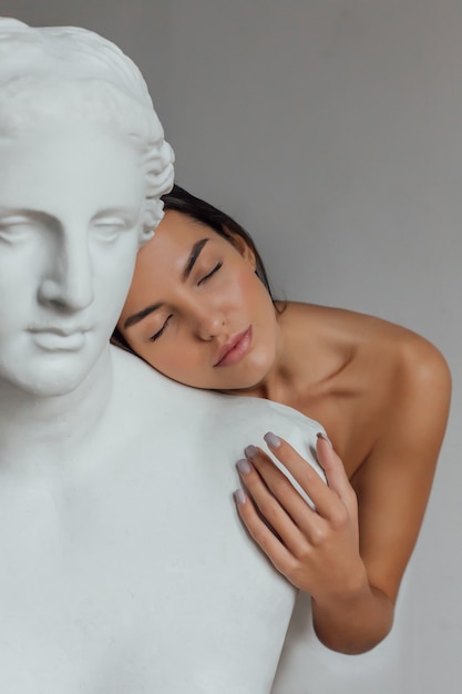 Une femme avec un visage et un corps bien soignés se tient près du buste d'une sculpture de femme