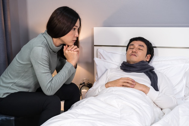 Femme visitant et prenant soin de son mari malade pendant qu'il dort sur le lit à la maison