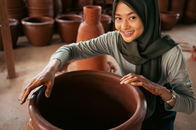 Femme voilée souriant tout en faisant des pots en argile sur roues