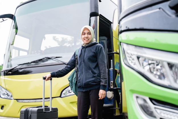 Une femme voilée sourit en regardant la caméra tout en tenant une valise du bus avant de partir