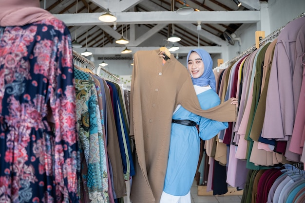 Une femme voilée tient une robe à montrer en se tenant debout