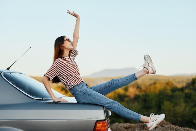 Une femme avec une voiture s'est arrêtée sur la route pour se reposer pendant le voyage a levé les bras et les jambes du bonheur et d'un beau paysage