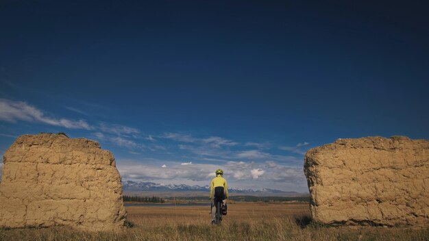 La femme voyage sur un terrain mixte cyclotourisme avec bikepacking Le voyage du voyageur avec des sacs à vélo Sport bikepacking bike sportswear dans les couleurs vert noir Montagne enneigée arche de pierre