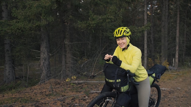 La femme voyage sur un terrain mixte cyclotourisme avec vélo bikepacking outdoor Le voyage du voyageur avec des sacs à vélo Élégant bikepacking bike sportswear dans les couleurs vert noir Magic forest park