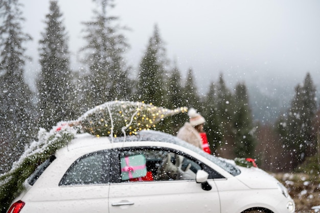 Une femme voyage en voiture avec des cadeaux et un sapin de noël sur la route de montagne