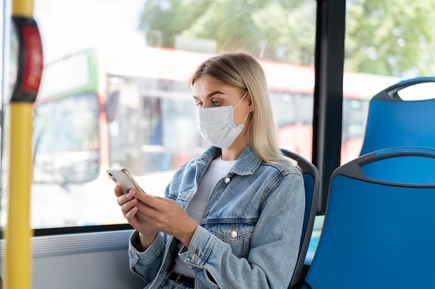 Femme voyageant en bus public utilisant un smartphone tout en portant un masque médical pour se protéger