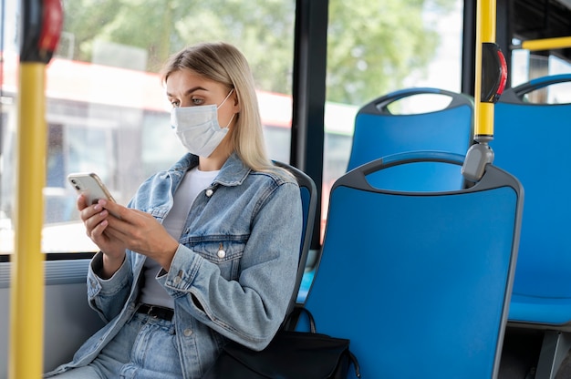 Femme voyageant en bus public utilisant un smartphone tout en portant un masque médical pour se protéger