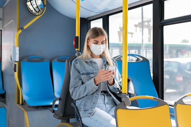 Femme voyageant en bus public utilisant un smartphone tout en portant un masque médical pour se protéger