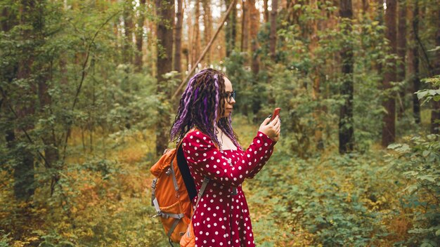 Femme voyageant avec des dreadlocks avec un téléphone dans les bois Voyageuse avec sac à dos dans les bois lisant la carte sur un smartphone et cherchant un moyen par temps nuageux