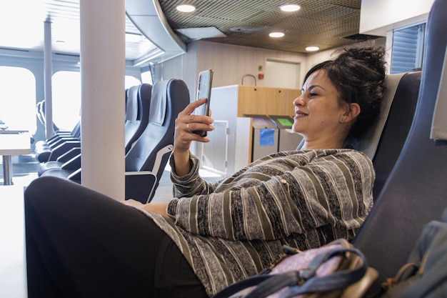 Femme voyageant en ferry assis souriant et regardant un téléphone portable