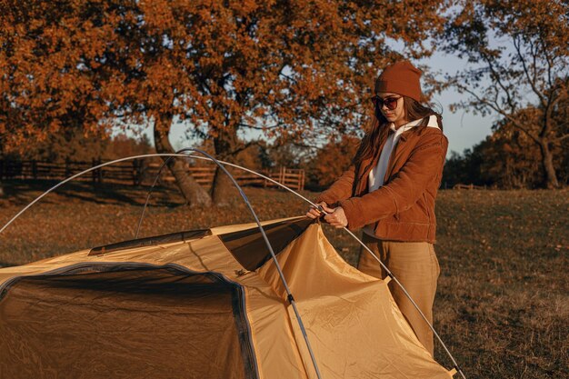 Femme voyageant installant ou montant une tente de camping dans la forêt d'automne