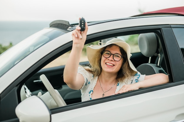 Femme voyageant tenant les clés de la nouvelle voiture et souriant à la propriété de l'appareil photo et acheter le concept automobile