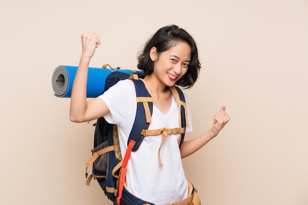 Femme voyageur asiatique sur mur isolé célébrant une victoire