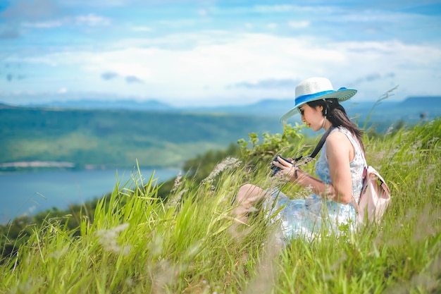 Femme voyageur assis sur l&#39;herbe et prenant une vue photo du barrage et de la montagne