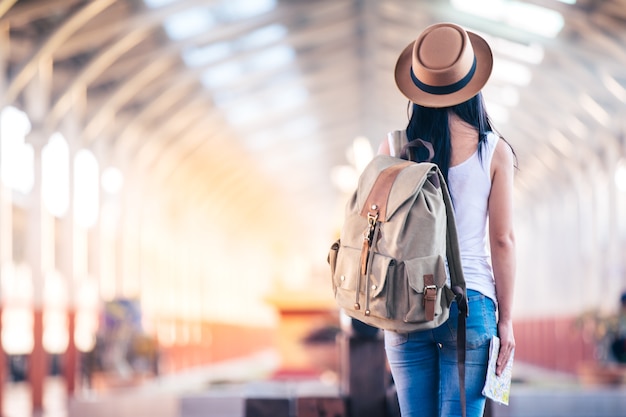Femme voyageur avec chapeau et sac à dos, voyageant avec carte papier sur la gare.