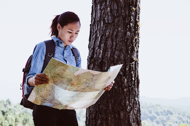 Femme voyageur heureux avec sac à dos et la recherche de la bonne direction sur la carte près de montagnes incroyables et vue sur la forêt.