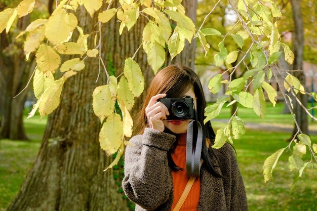 Femme de voyageur prenant la photographie avec son appareil photo dans le parc, journée ensoleillée d&#39;automne