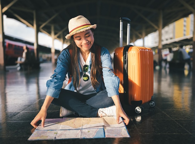 Femme voyageur touriste look carte avec sac à dos et valise orange à la gare