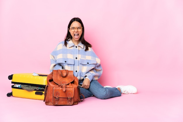 Femme de voyageur avec une valise assis sur le sol en criant à l'avant avec la bouche grande ouverte