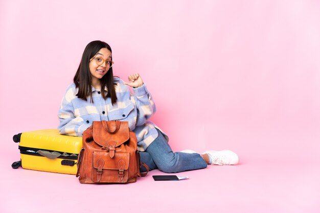 Femme de voyageur avec une valise assis sur le sol fier et satisfait de soi