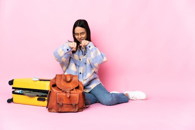 Femme de voyageur avec une valise assis sur le sol avec un geste de combat