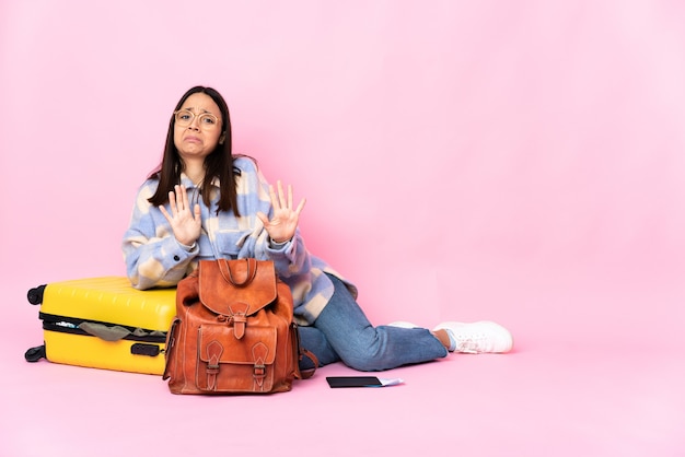 Femme de voyageur avec une valise assis sur le sol nerveux s'étendant les mains vers l'avant