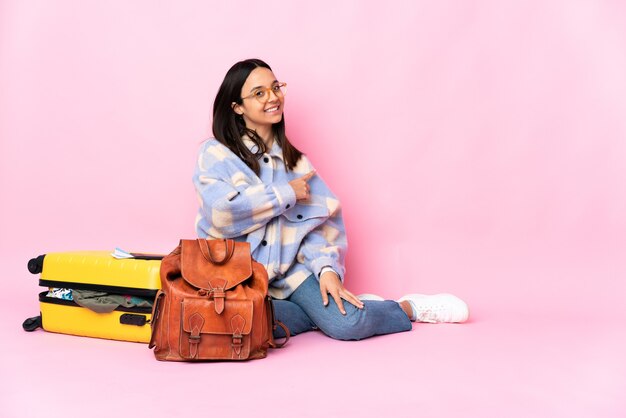 Femme de voyageur avec une valise assis sur le sol pointant vers l'arrière