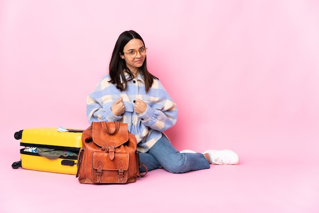 Femme de voyageur avec une valise assis sur le sol pointant vers soi