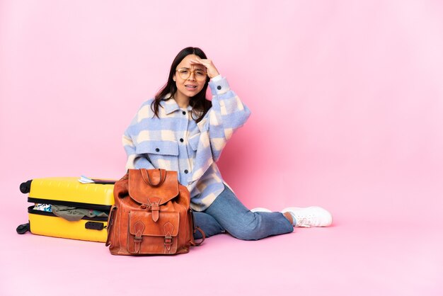 Femme voyageur avec une valise assis sur le sol à la recherche de loin avec la main pour regarder quelque chose