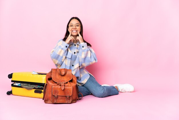 Femme de voyageur avec une valise assis sur le sol en souriant avec une expression heureuse et agréable